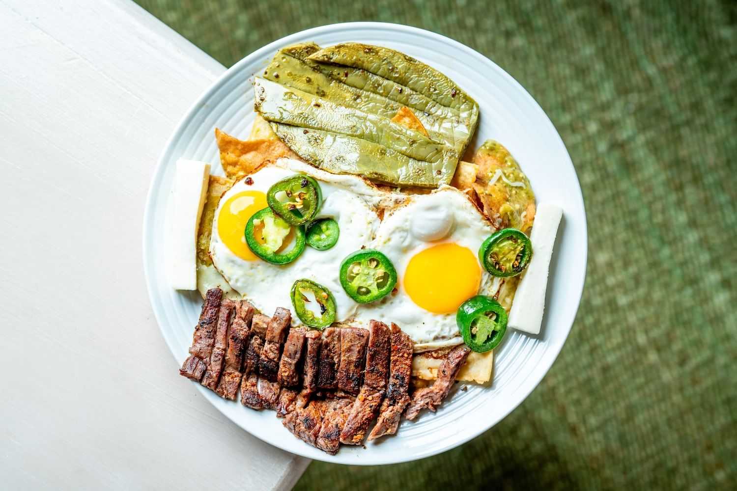 Plate of chilaquiles with fried eggs, jalapeños, grilled beef, and cactus paddles.