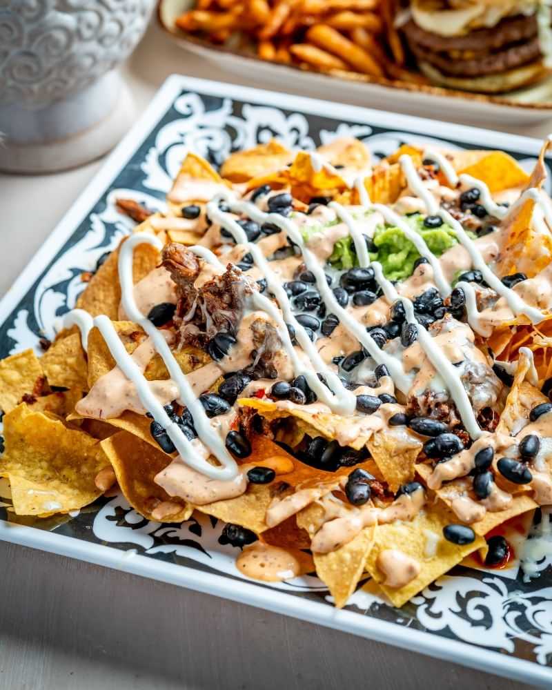 Plate of nachos topped with beans, cheese, and sauces, garnished with guacamole.
