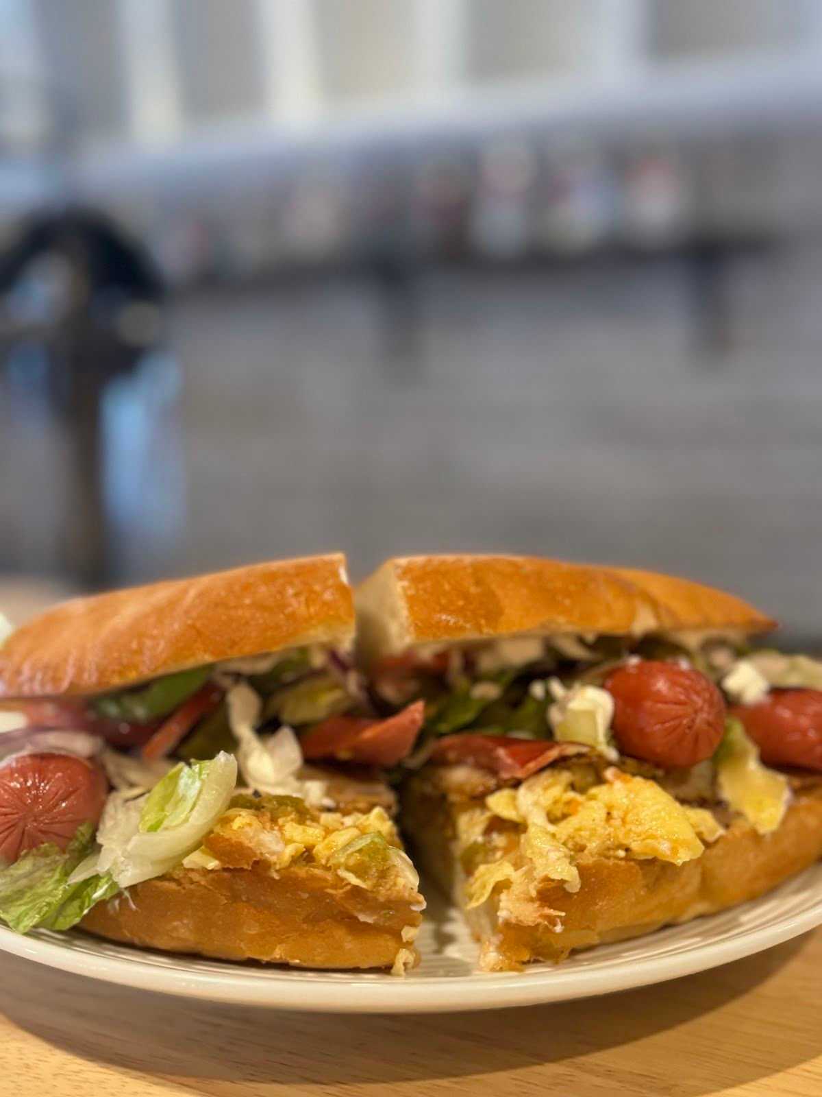 Close-up of a gourmet sandwich with vegetables, sliced sausage, and cheese on a white plate.
