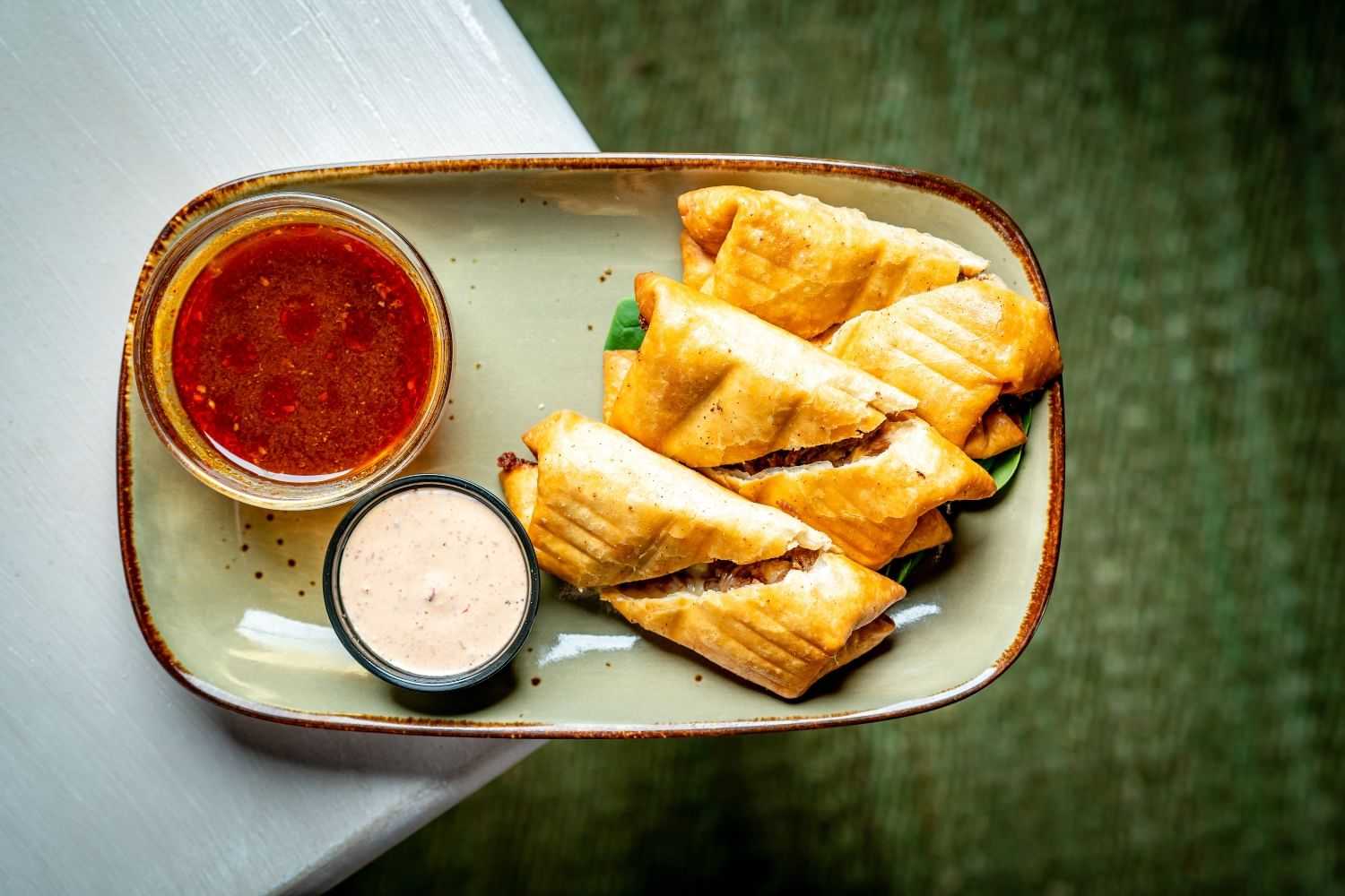 Crispy rolls with two dipping sauces on a rectangular plate.