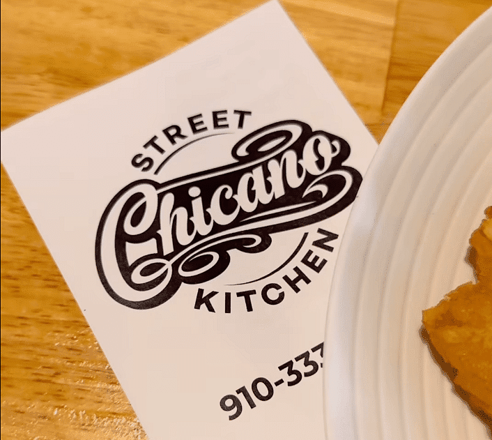 Street Chicano Kitchen menu with logo and contact number, part of a plate visible on the right.